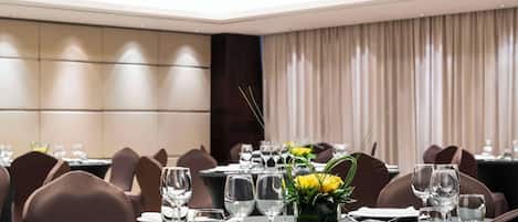 Comedor bien iluminado con mesas redondas dispuestas para una comida, con cristalería transparente y un centro de mesa con flores amarillas.