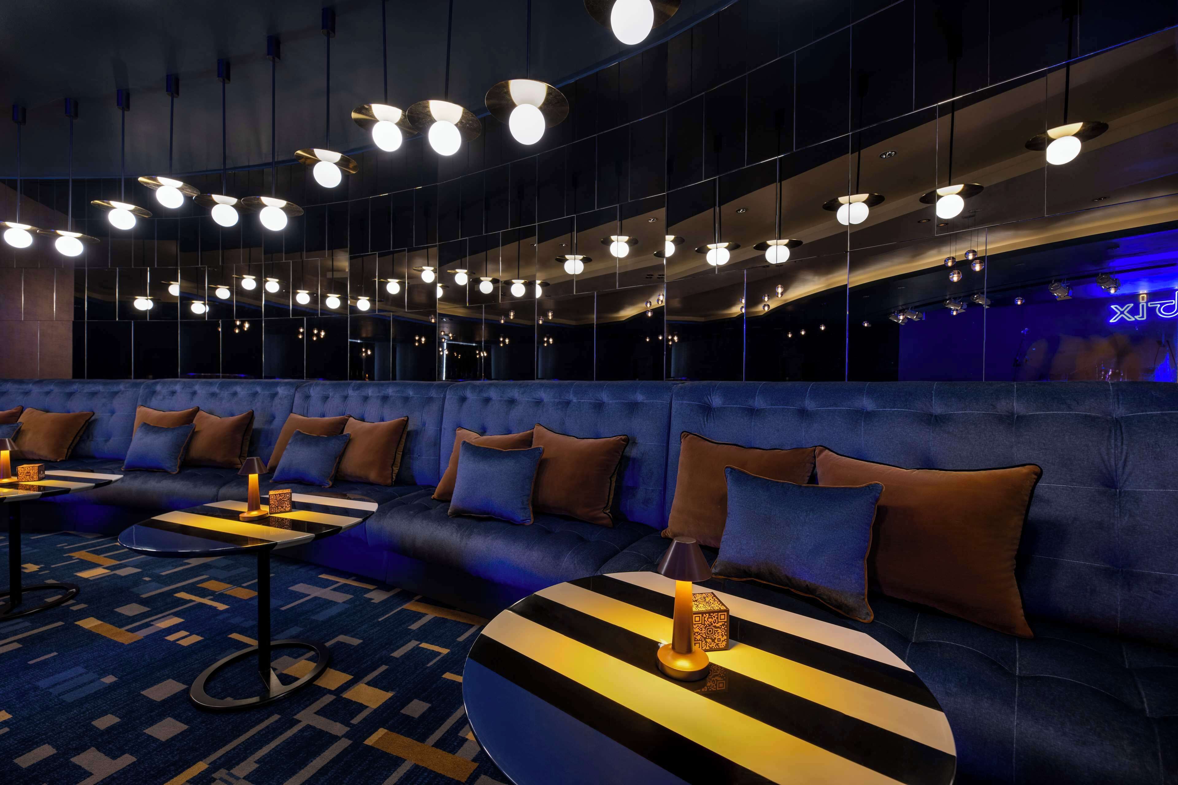 Ein stilvoller Lounge-Bereich mit blauem Sofa, runden Tischen und Hängelampen.