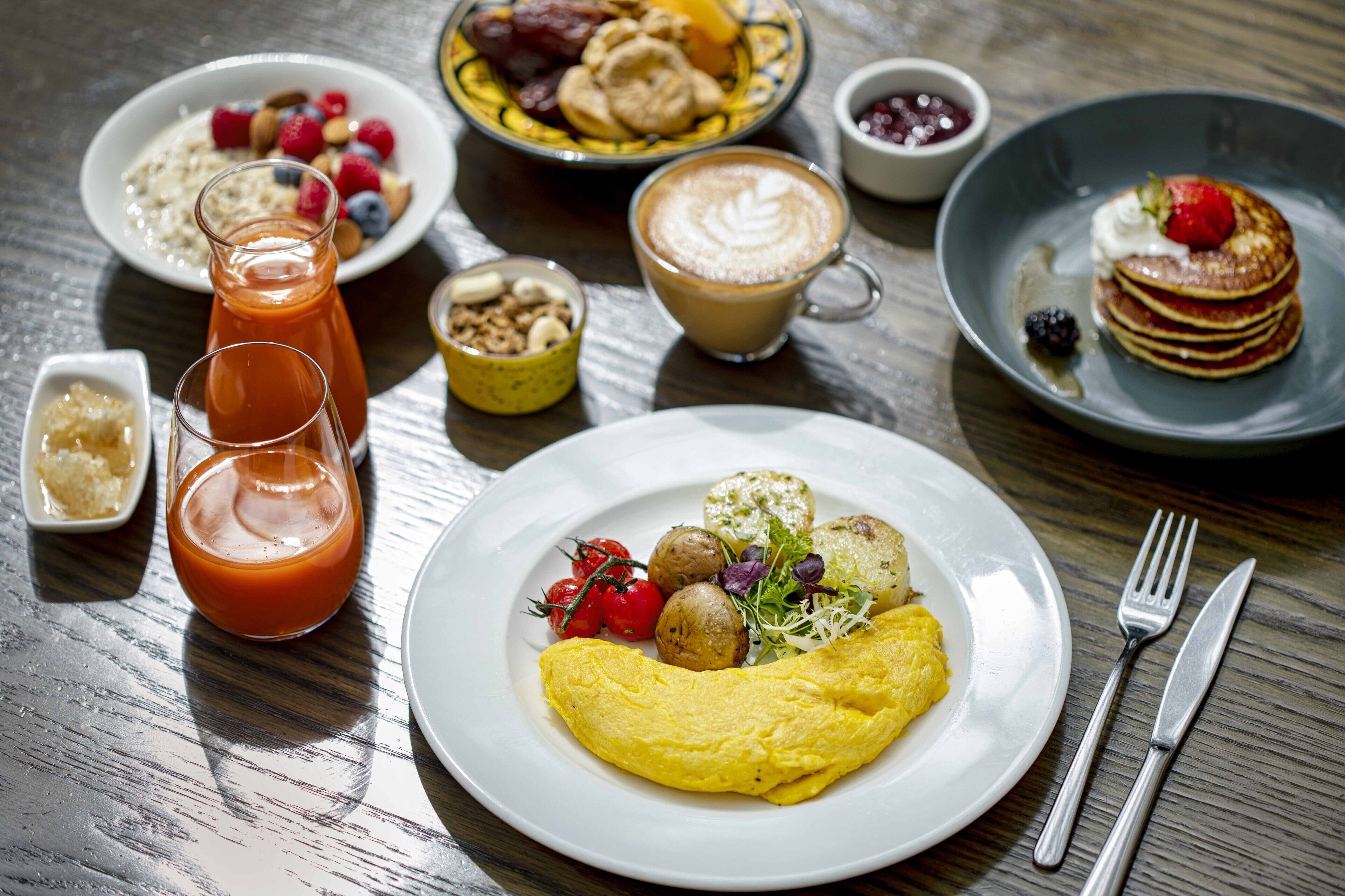 A breakfast setting with various dishes including an omelet, pancakes, and a coffee drink.