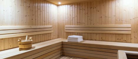 A wooden sauna with benches, a towel stack, and a wooden bucket with a towel.