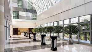 A spacious lobby with a high ceiling, large windows, and modern black tables with potted plants. - Hyatt Regency Oryx Doha (Doha)
