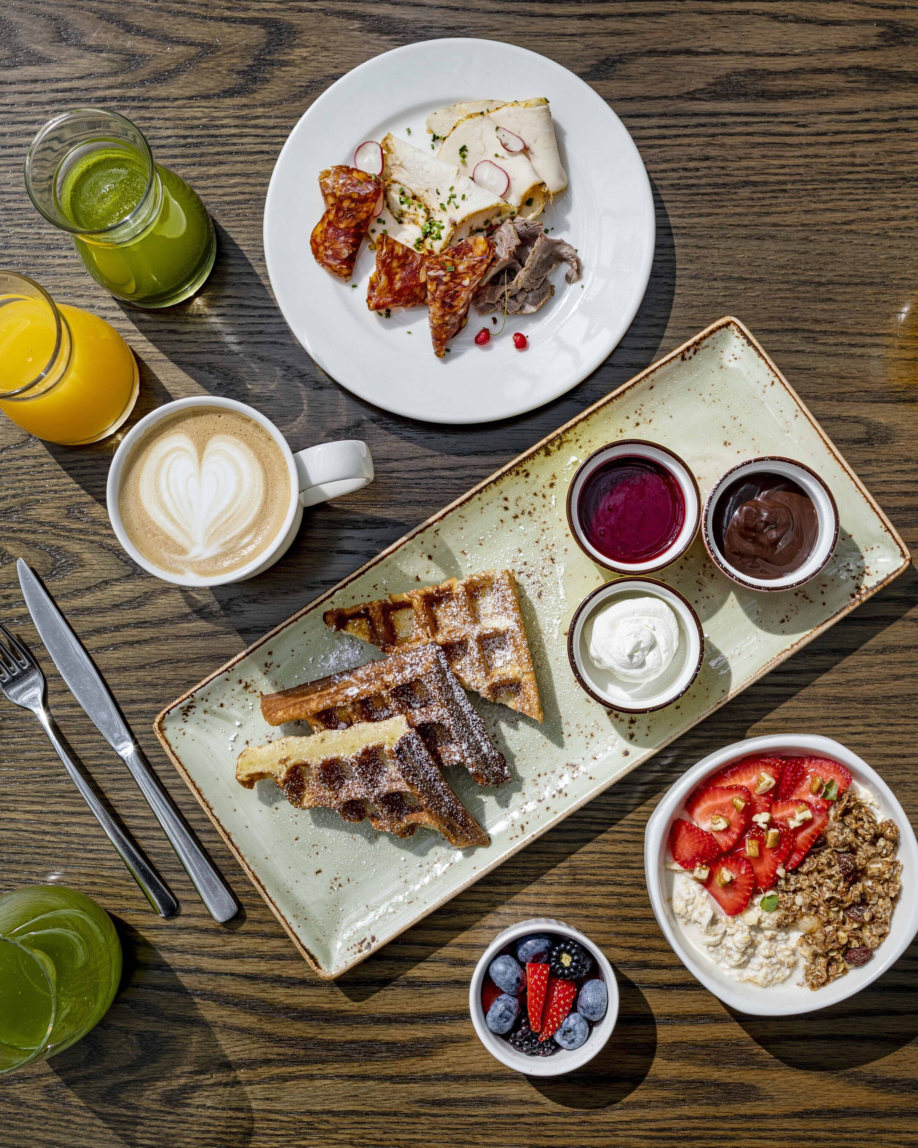 A breakfast setting with waffles, pancakes, and a variety of fruits and beverages on a wooden table.