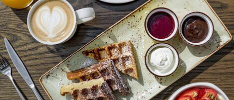 A breakfast setting with waffles, pancakes, and a variety of fruits and beverages on a wooden table.