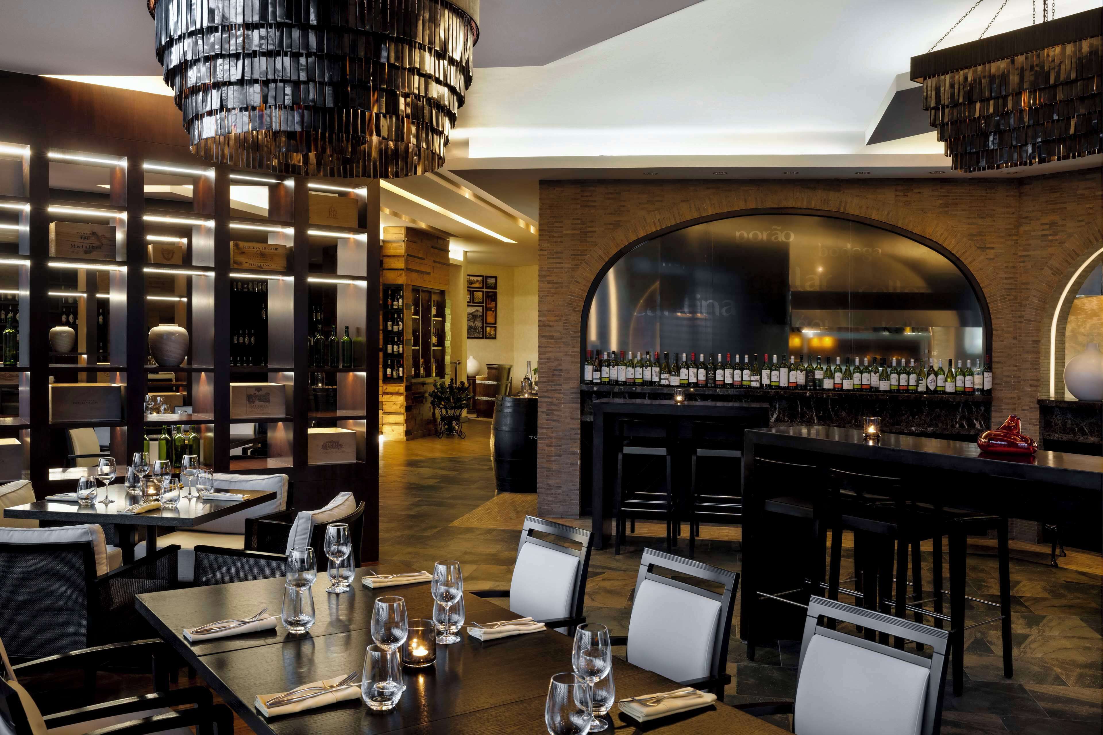 Un restaurante moderno con zona de bar, que presenta una pared de ladrillo, mesas de madera y una variedad de botellas en las estanterías.