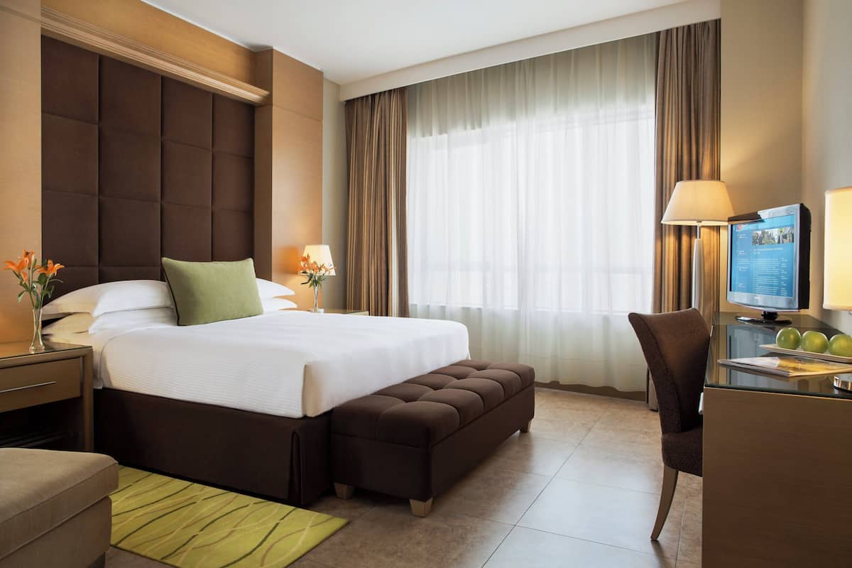 A hotel room with a large bed, a desk with a computer, and a chair.