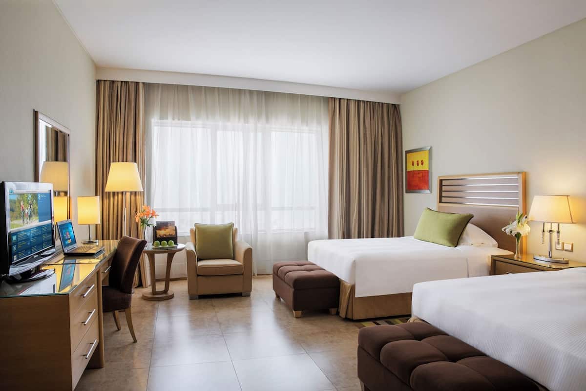 A hotel room with a desk, two beds, a chair, and a TV.