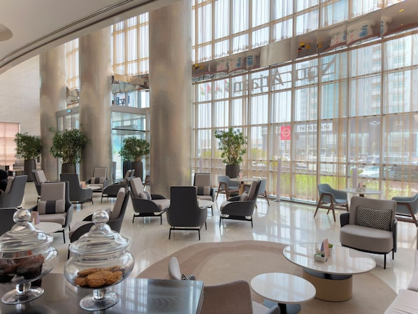 A spacious lobby with modern furniture, large windows, and indoor plants.