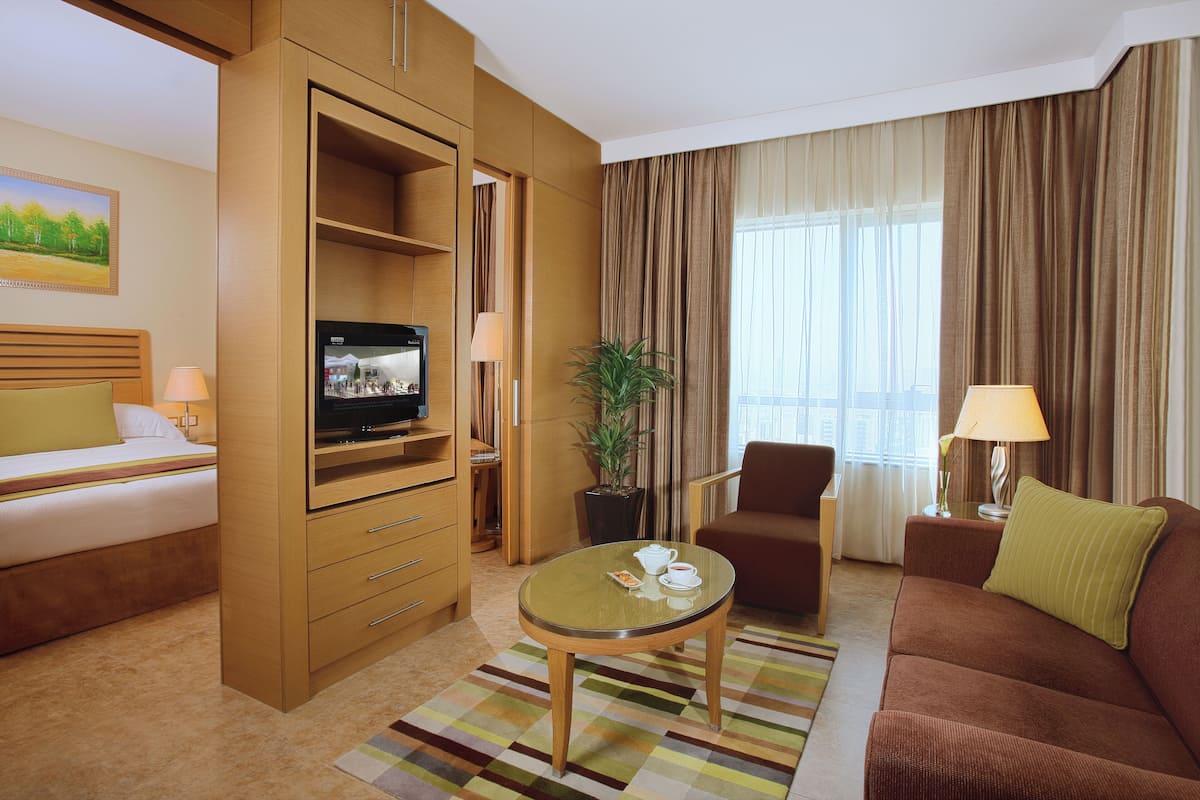 A hotel room with a bed, a TV, a sofa, a coffee table, and a plant.