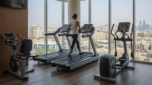 A gym with treadmills, an elliptical, and a stationary bike, with a cityscape view through large windows.