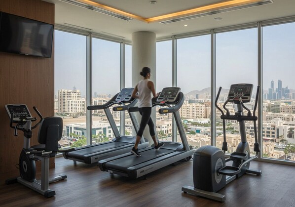A gym with treadmills, an elliptical, and a stationary bike, with a cityscape view through large windows.