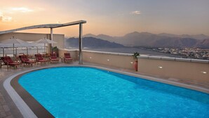 A swimming pool with lounge chairs and umbrellas, overlooking a mountainous landscape.