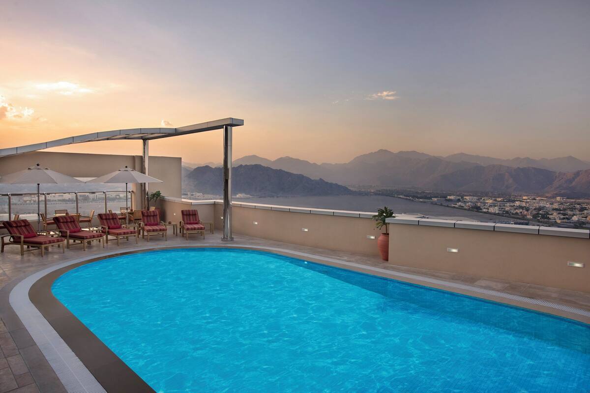A swimming pool with lounge chairs and umbrellas, overlooking a mountainous landscape.