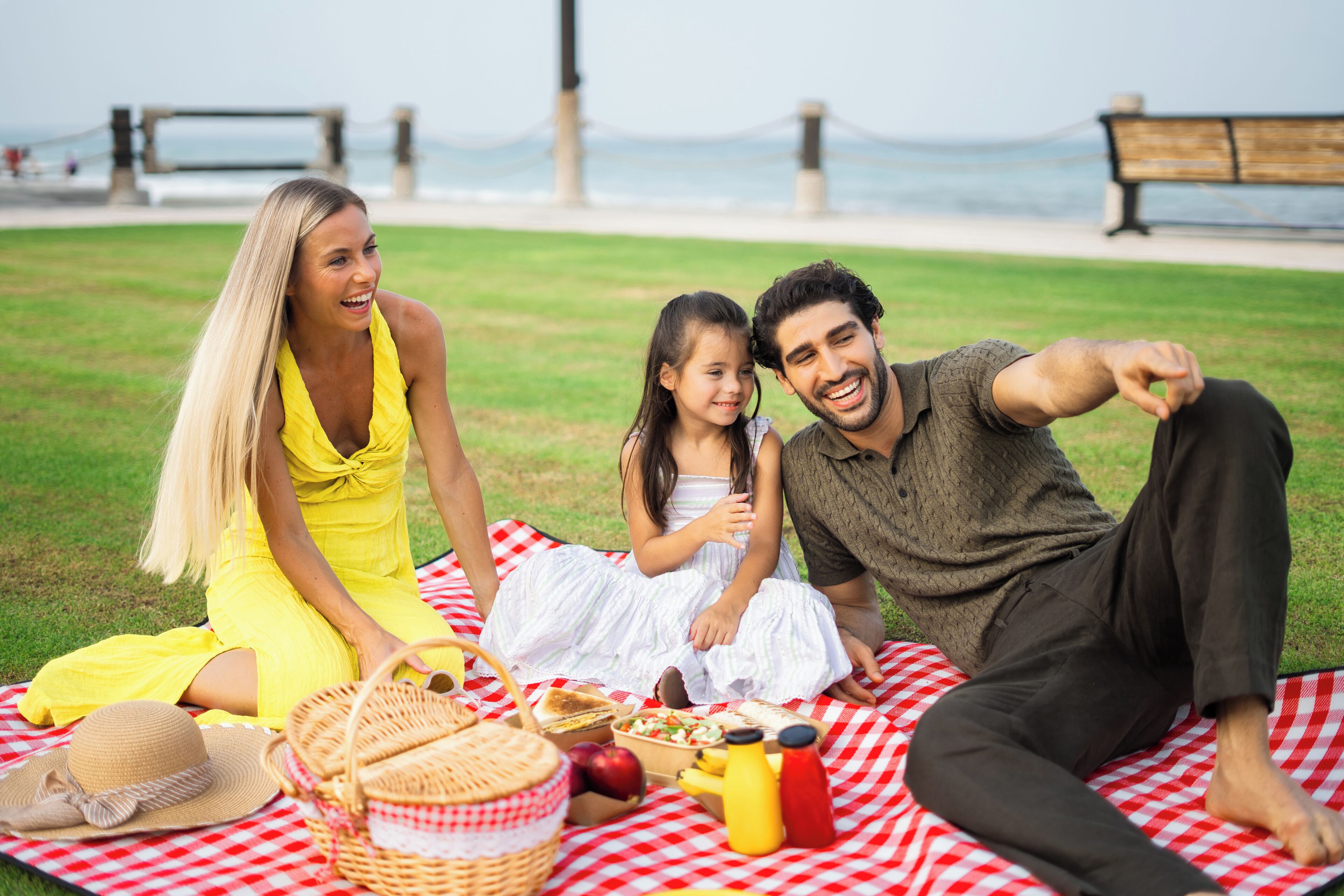 A family on a picnic blanket with food and drinks, a hat, and a basket.