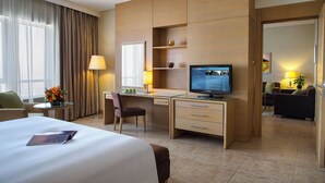 Une chambre d’hôtel avec un lit, un bureau avec un ordinateur, une chaise, une télévision et une petite table avec une lampe et des fleurs.