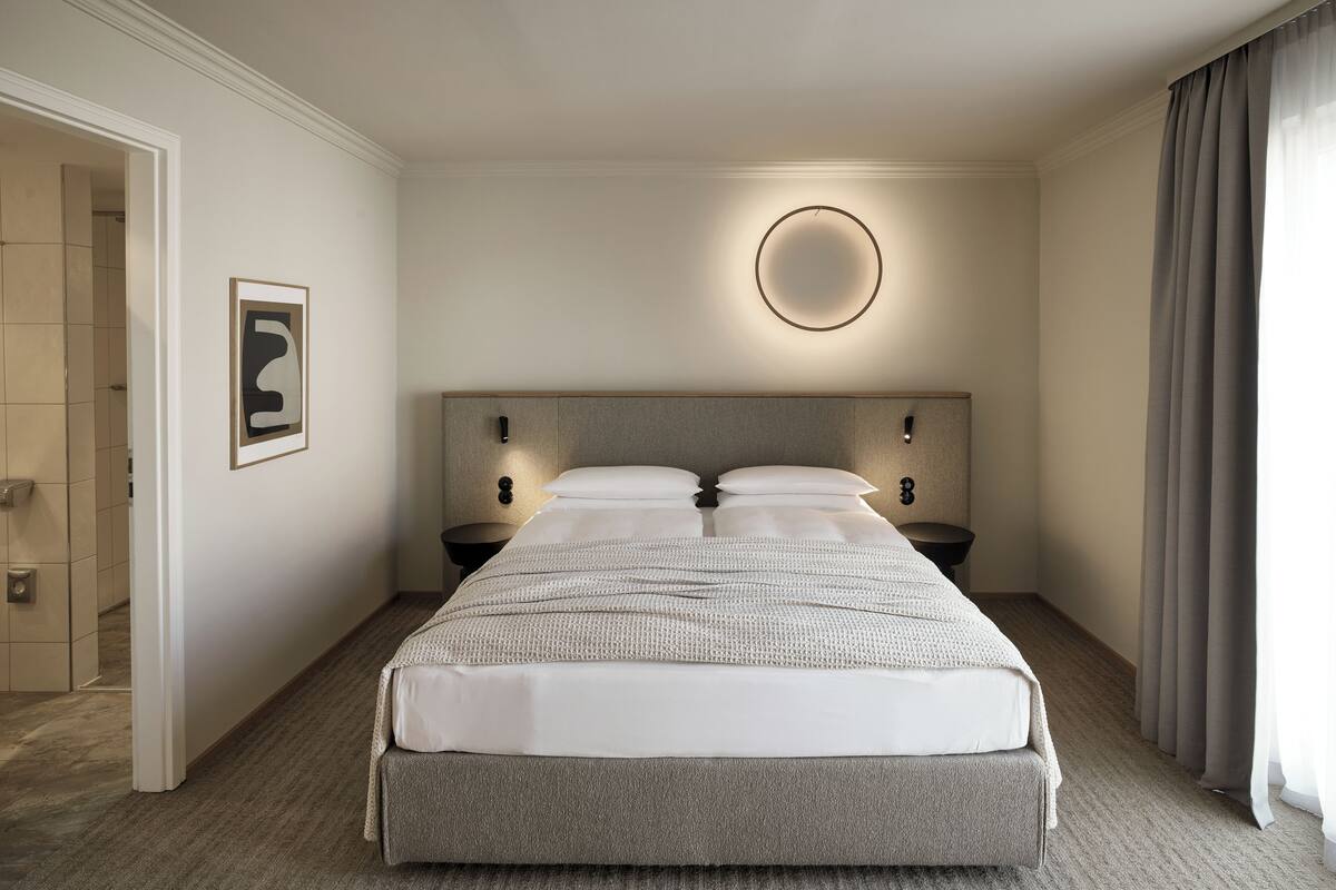 A hotel room with a large bed, two bedside tables, a wall-mounted light, and a framed picture on the wall.