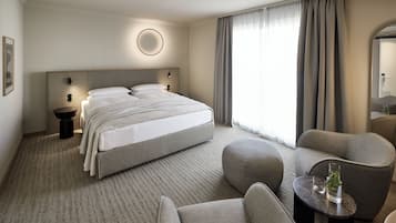 A modern hotel room with a large bed, a round wall light, a round mirror, and a seating area with a small table and chairs.
