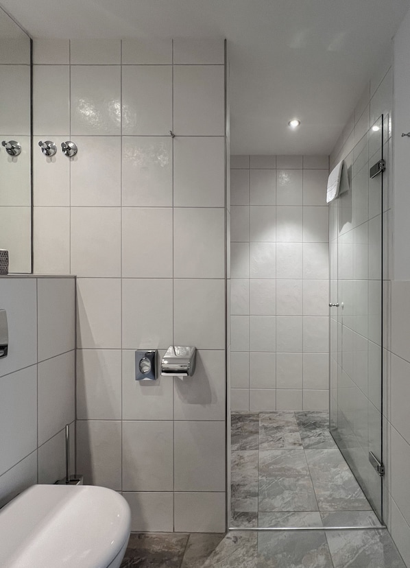 A modern bathroom with a toilet, a hand dryer, and a glass shower enclosure.