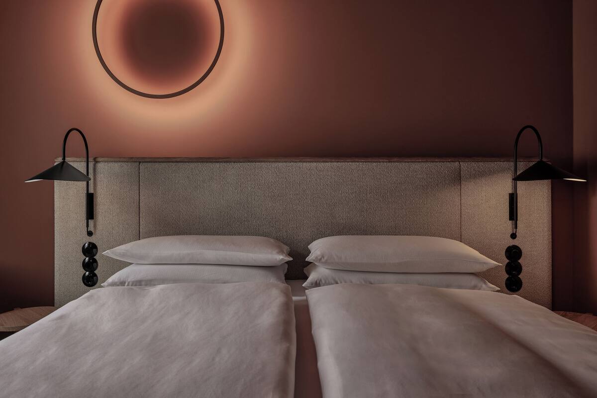 A double bed with a textured headboard, two bedside lamps, and a circular wall light fixture.