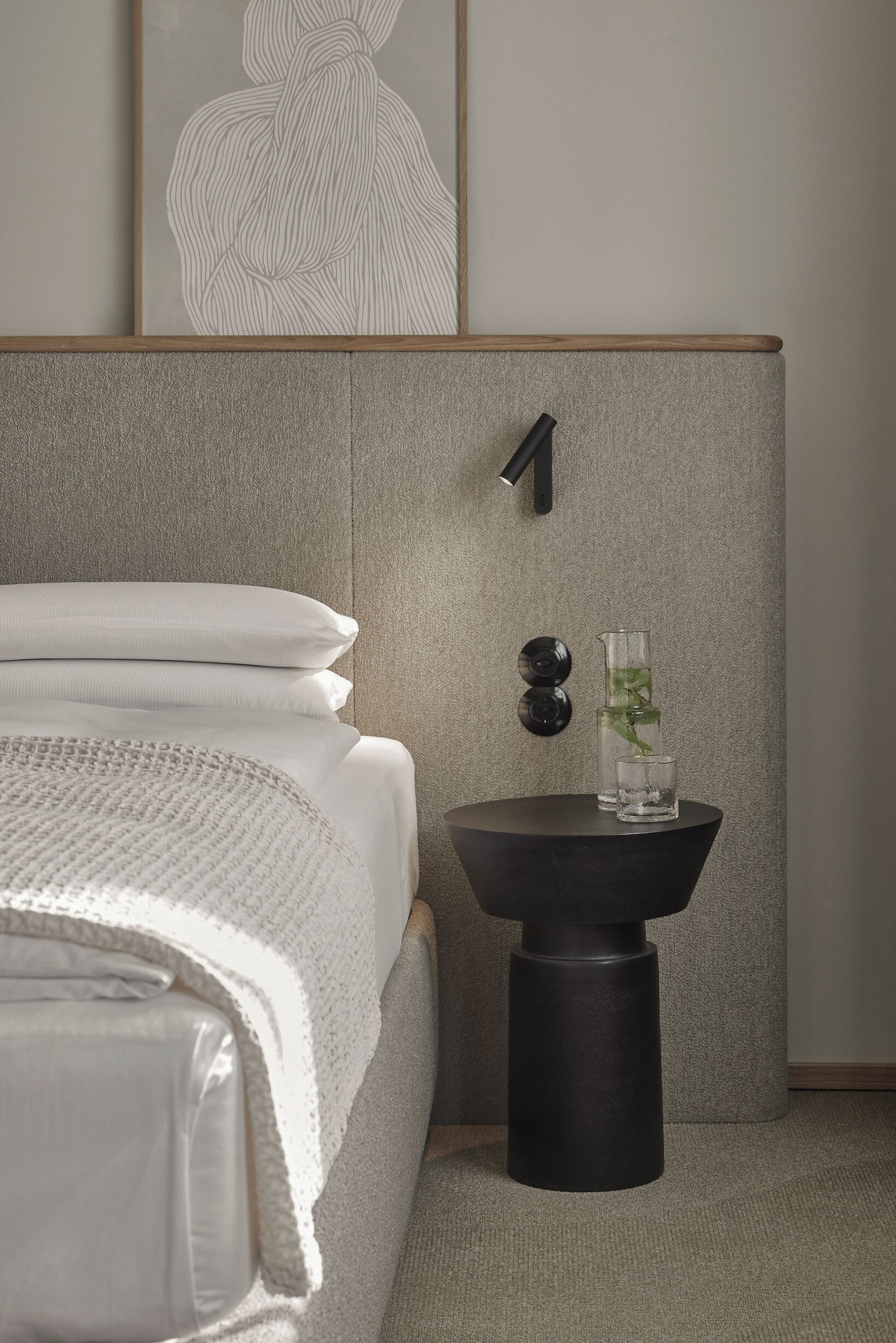 A neatly made bed with white linens, a small black side table with a glass vase and a plant, and a wall-mounted number '1' sign.