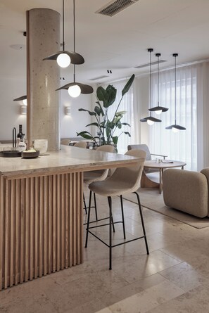 Una cocina moderna con una isla central, taburetes de bar, iluminación colgante y una planta grande.