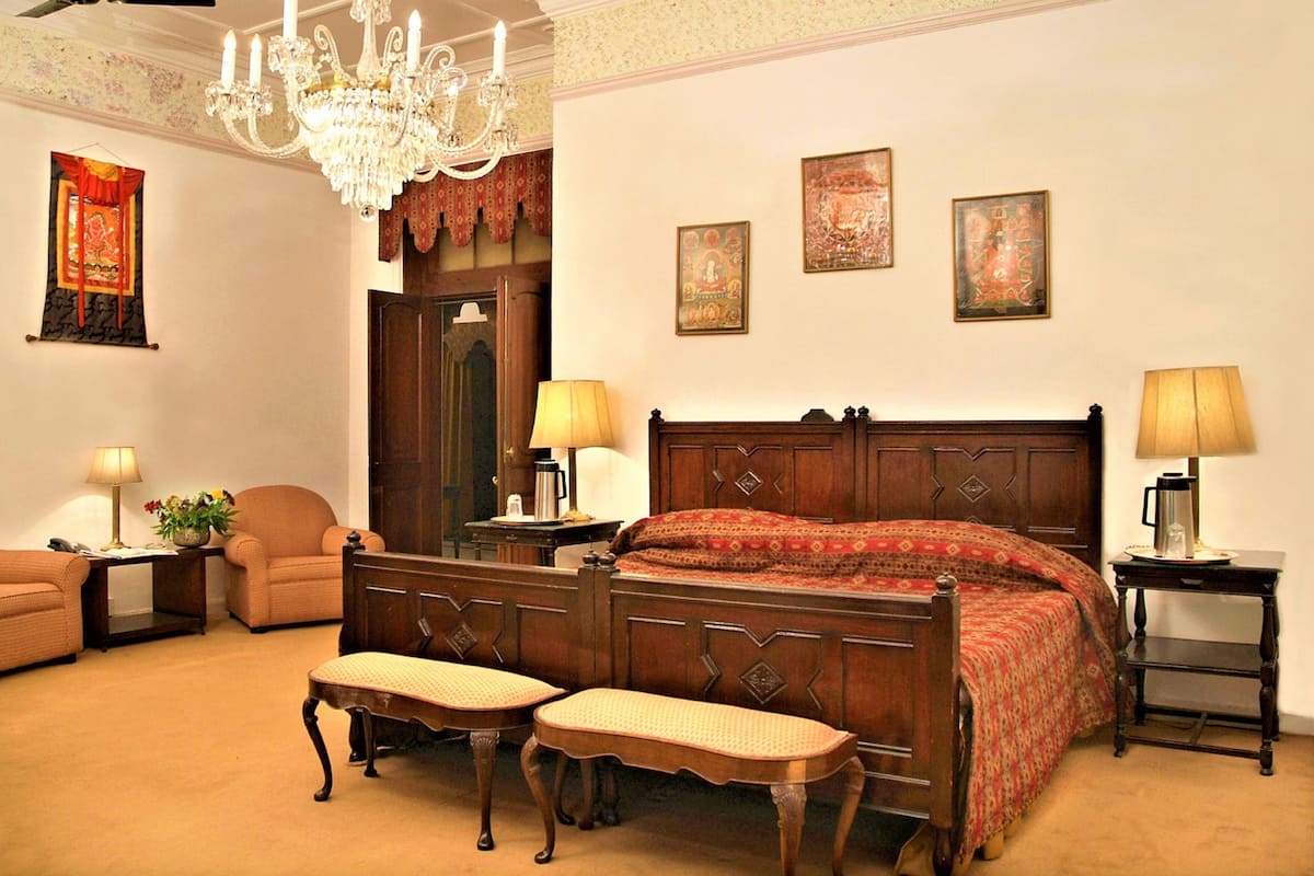 Een klassieke slaapkamer met een houten bed, twee nachtkastjes met lampen, een bankje en een kroonluchter.
