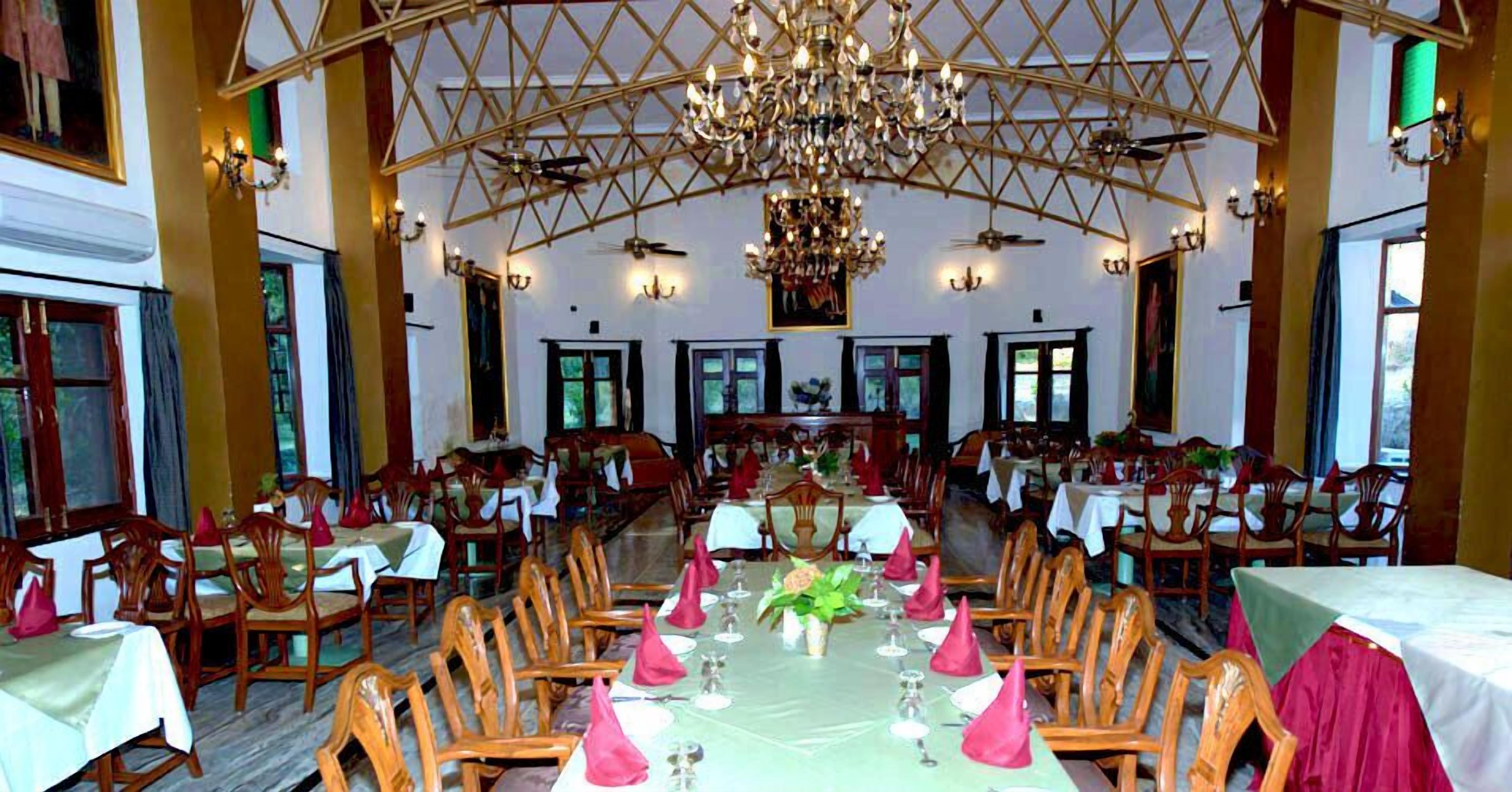 A large dining hall with multiple tables set for a meal, a chandelier, and a high ceiling with a geometric pattern.