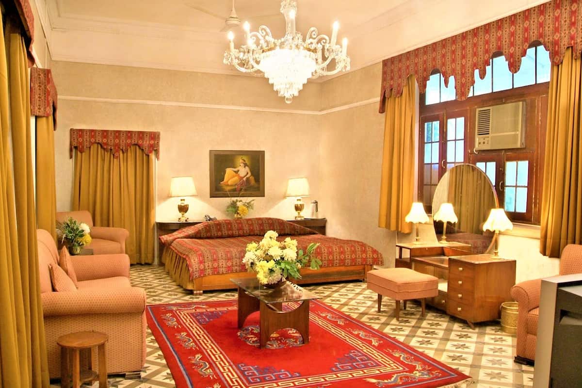 Een hotelkamer met een groot bed, twee nachtkastjes met lampen, een bank, een kleine tafel met bloemen, een spiegel en een televisie.