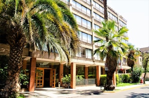 A hotel with a modern facade, large windows, and palm trees in front. - Hotel Casa Nogales (Santiago)