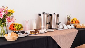 Ett bord med ett stort urval av mat, kaffemaskiner och en vas med blommor.
