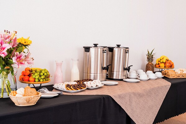 A buffet table with various food items, coffee makers, and a vase of flowers. - Hotel Casa Nogales (Santiago)