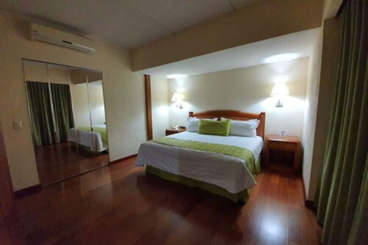 A hotel room with a bed, bedside tables, a mirror, and a wooden floor.