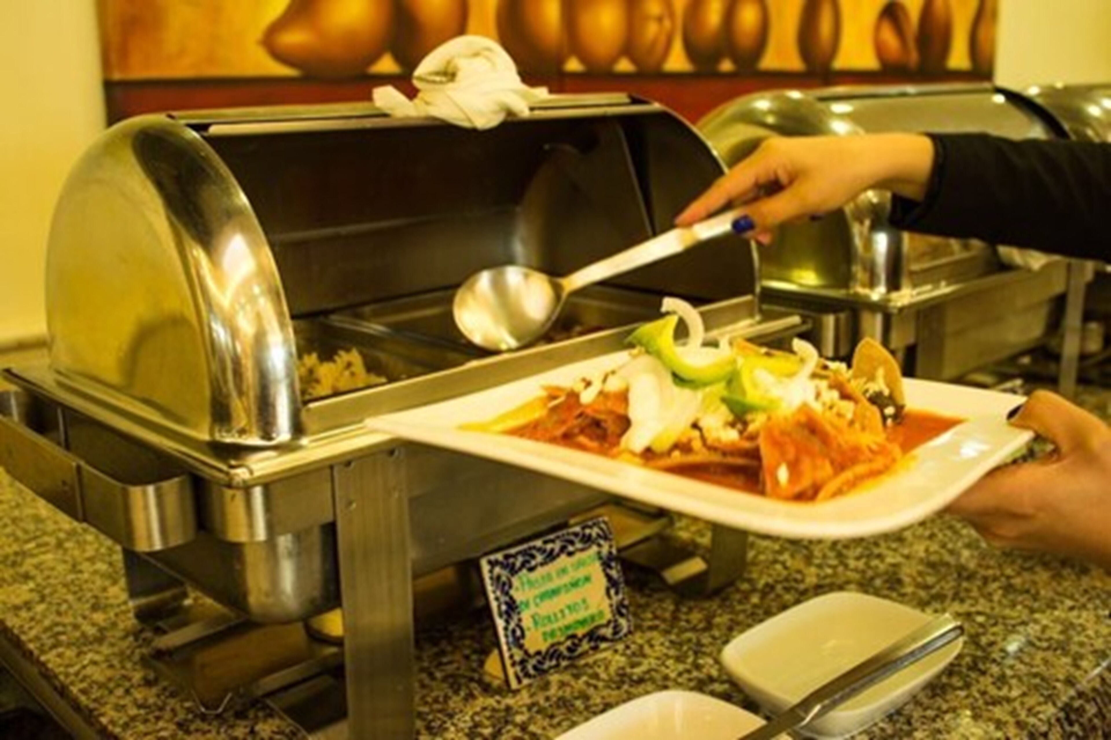 Una barra de buffet con una parrilla cubierta, utensilios para servir y un plato de comida.
