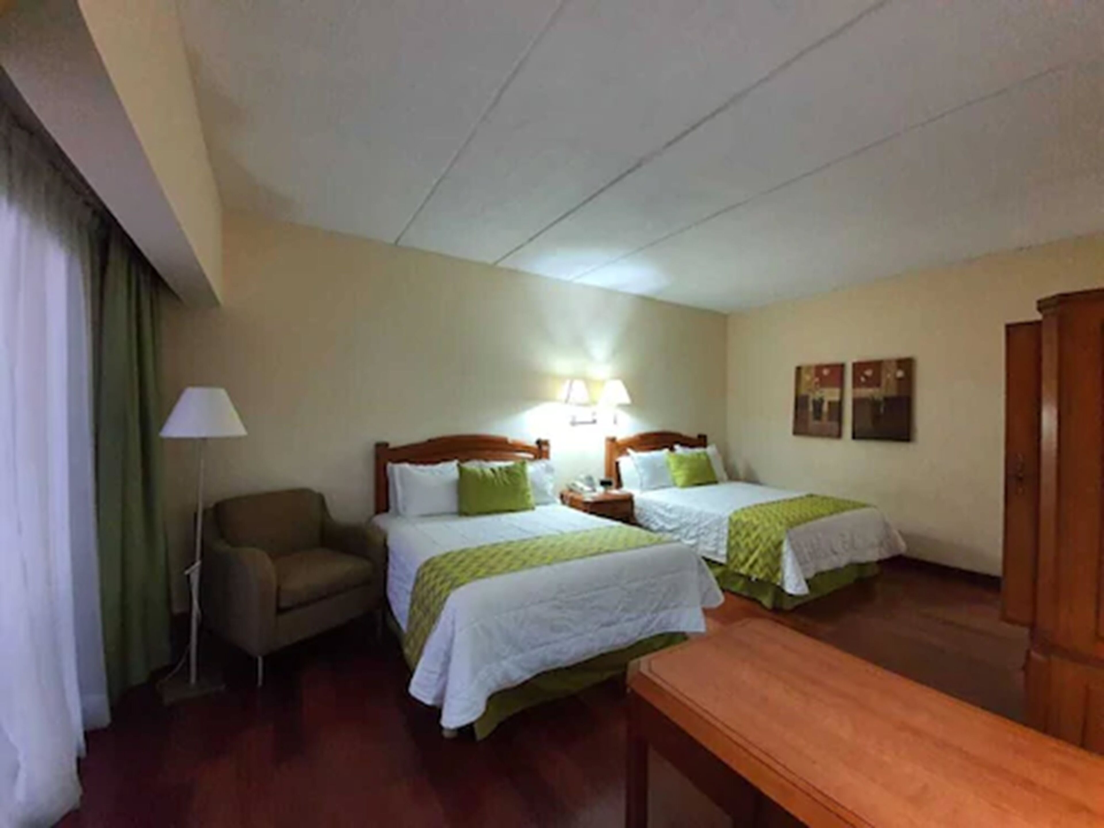 A hotel room with two beds, a chair, a desk, and a wardrobe.