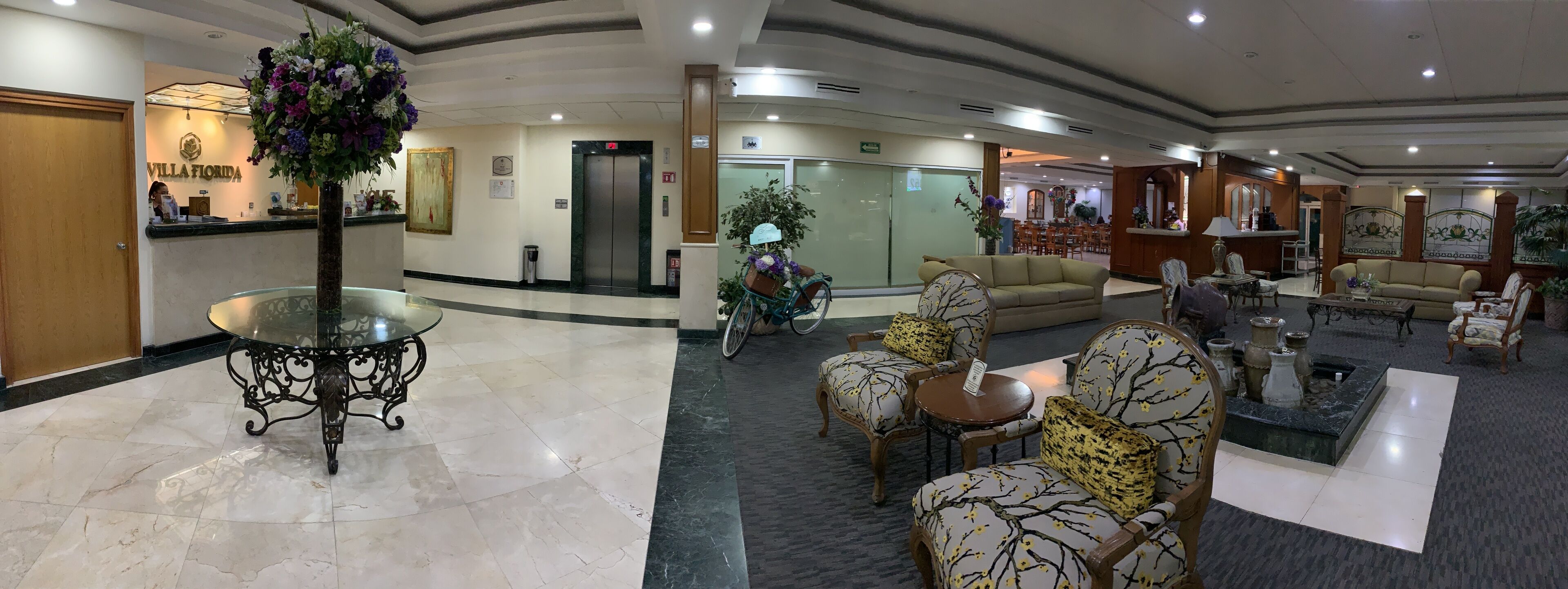 A hotel lobby with a reception desk, seating area, and a dining section.