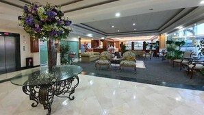 Un vestíbulo de hotel con una mesa de vidrio, un centro de mesa floral, una zona de estar y una recepción.