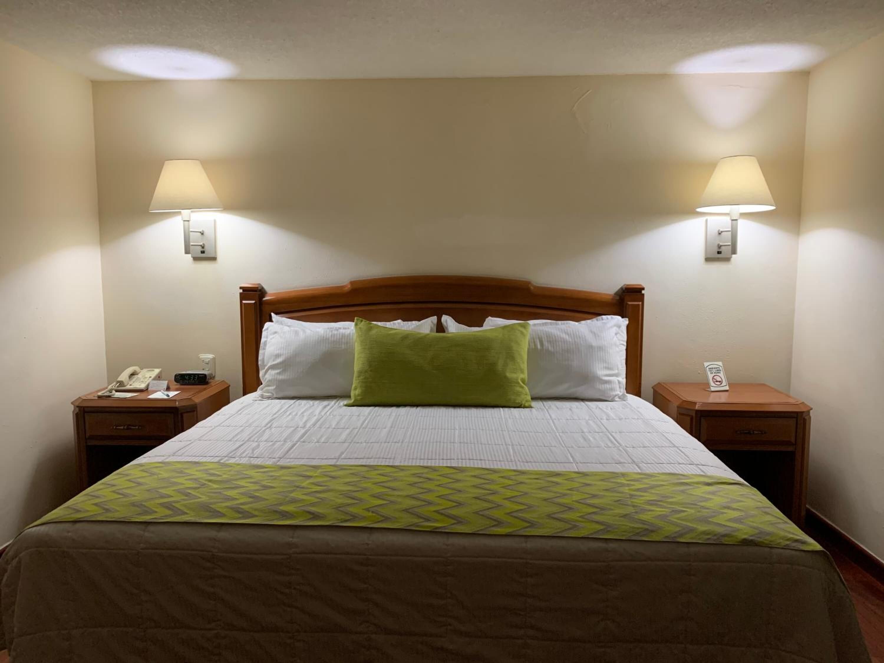 Habitación de hotel con cama de madera, dos lámparas de noche, un teléfono y una señal en la mesita de noche.