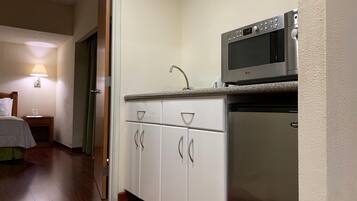 Cocina pequeña con armarios blancos, microondas y refrigerador.