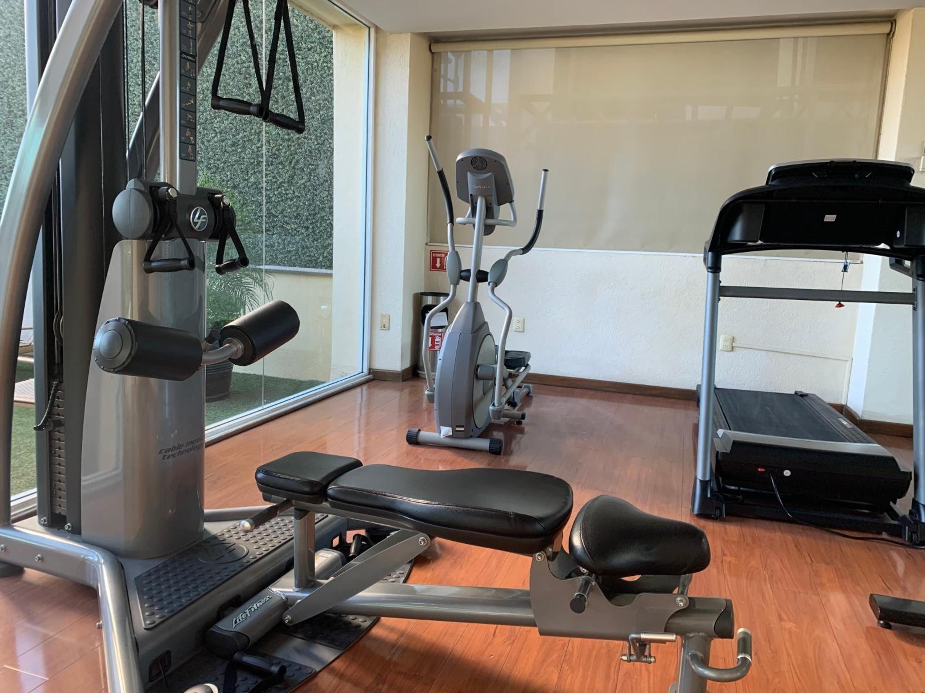 Un gimnasio con una prensa de banca, una elíptica y una cinta de correr.
