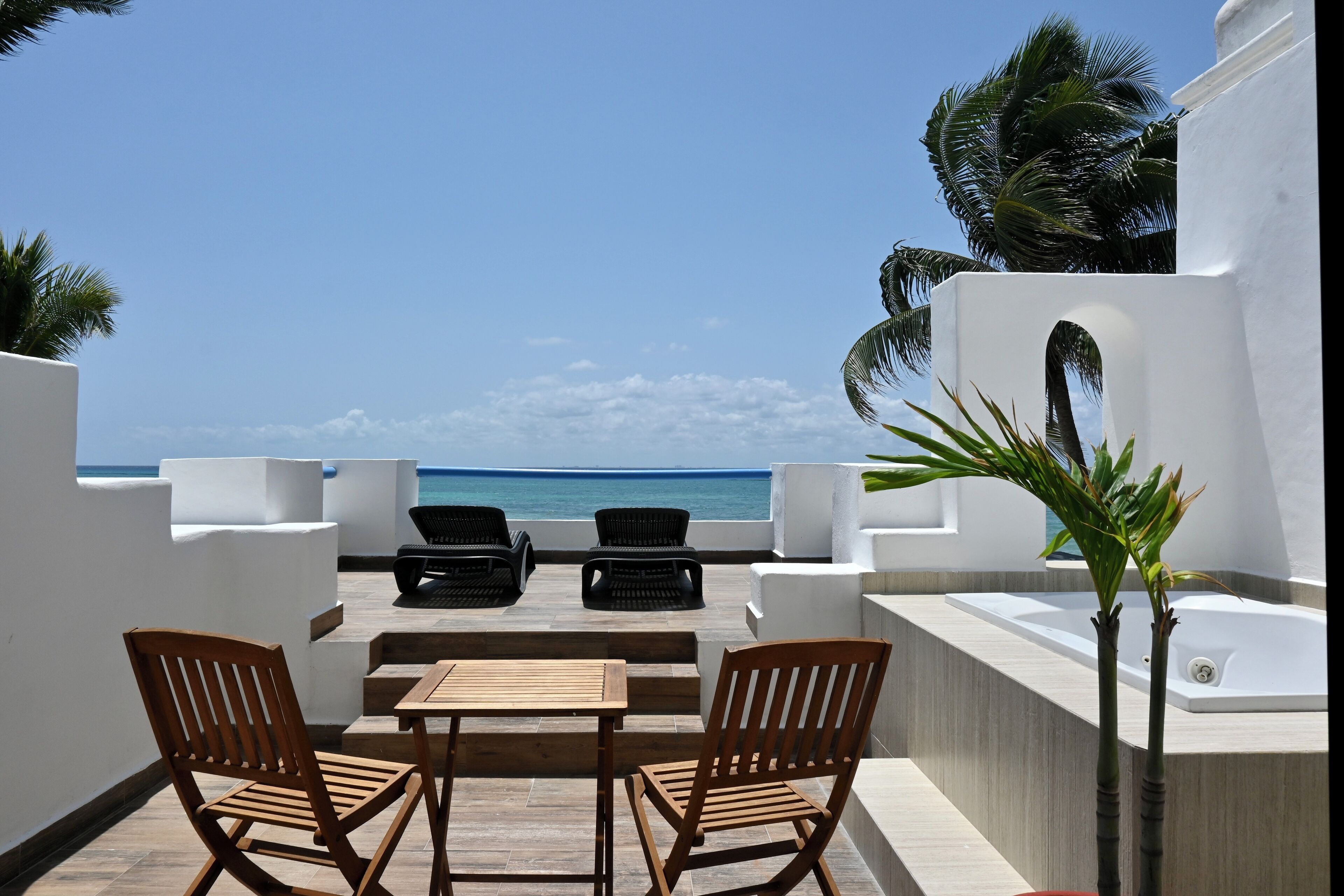 A terrace with two wooden chairs, a table, and a white bathtub.