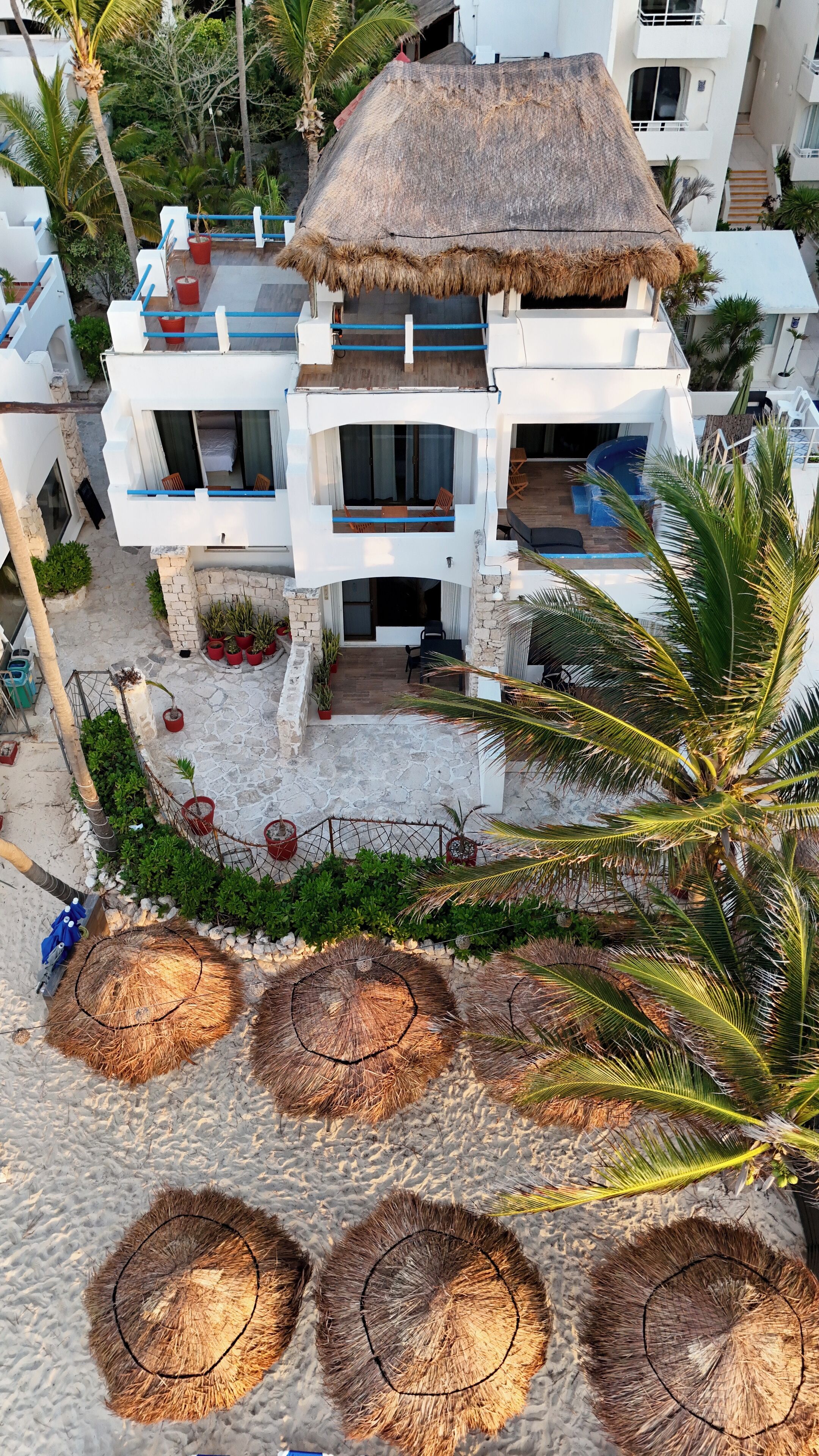A white building with a thatched roof, multiple balconies, and a pool area.