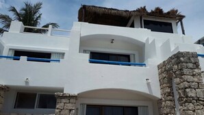 A two-story building with a white exterior, stone accents, and a thatched roof on the upper level. - Pelicano Inn Playa del Carmen - Beachfront Hotel (Playa del Carmen)