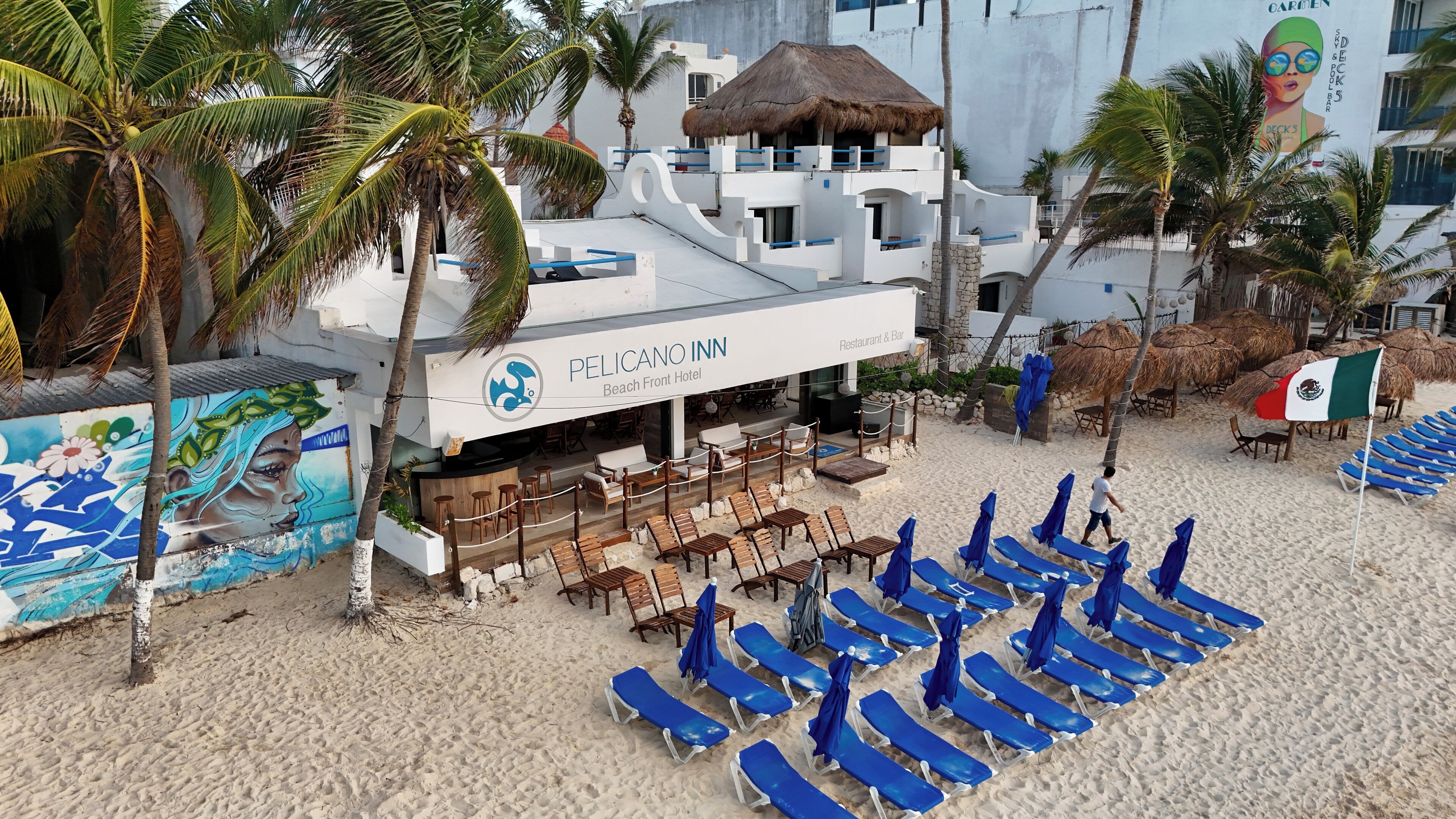 A beach front hotel with a restaurant and bar, lounge chairs, and palm trees.