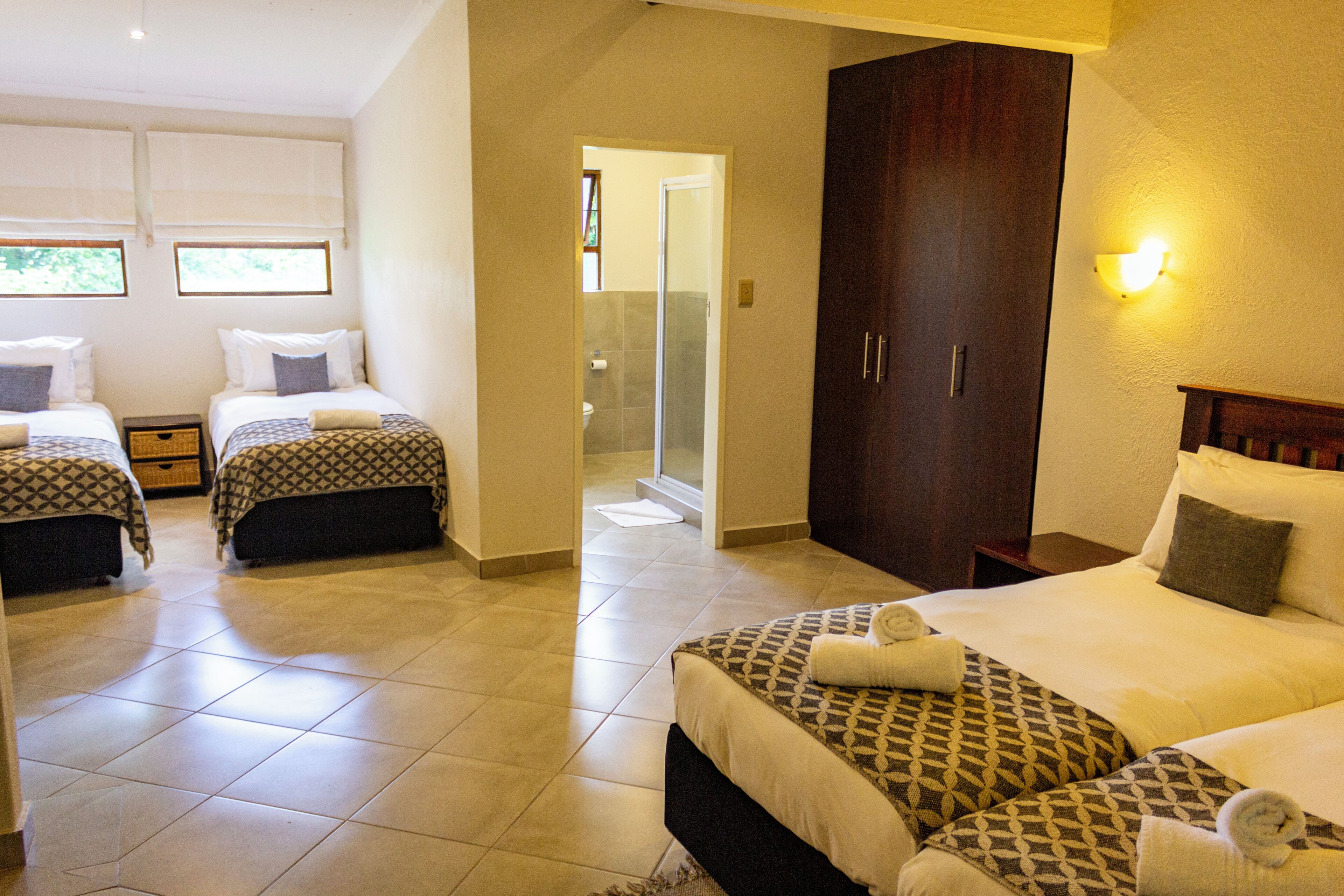 A hotel room with two single beds and one double bed, a wardrobe, and a bathroom visible through an open door.