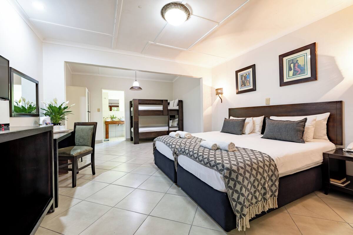 Une chambre d’hôtel avec un lit, un bureau, une chaise et une petite table avec une lampe.