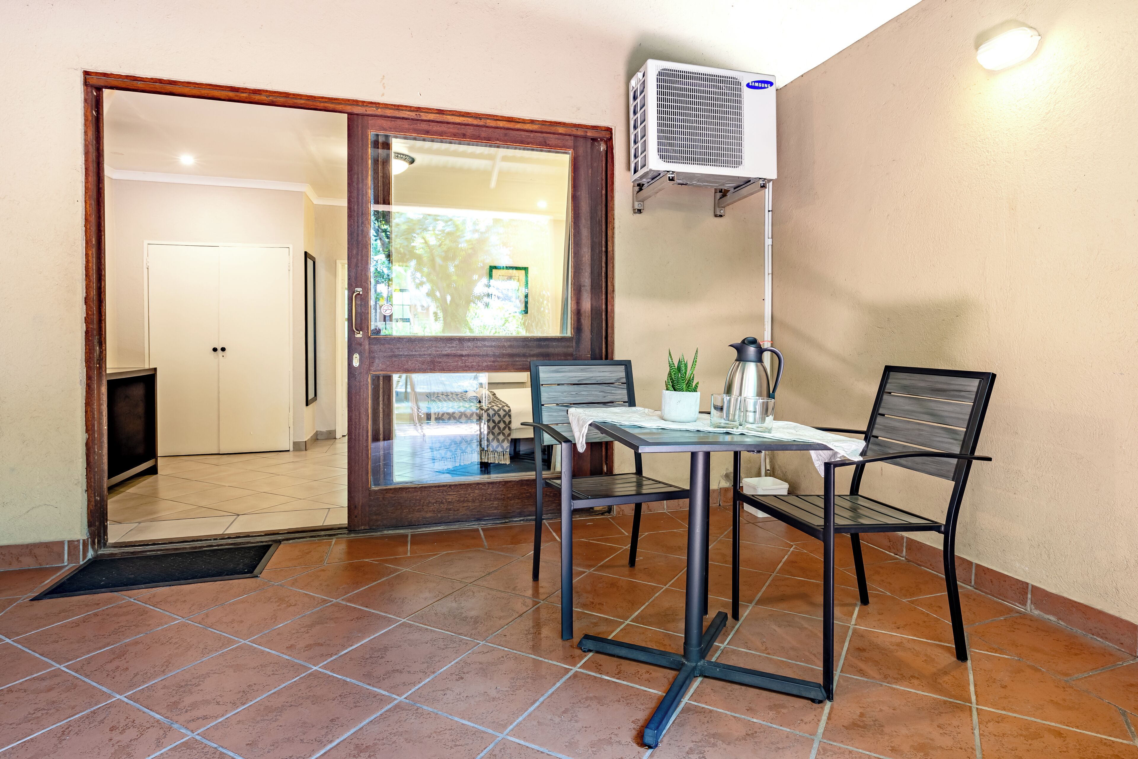 A room with a tiled floor, a table with chairs, a potted plant, a coffee maker, and a wall-mounted air conditioner.