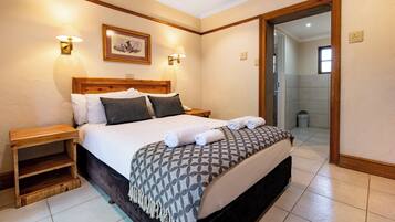 A neatly made bed with a patterned throw, a wooden nightstand, and a wall-mounted lamp.