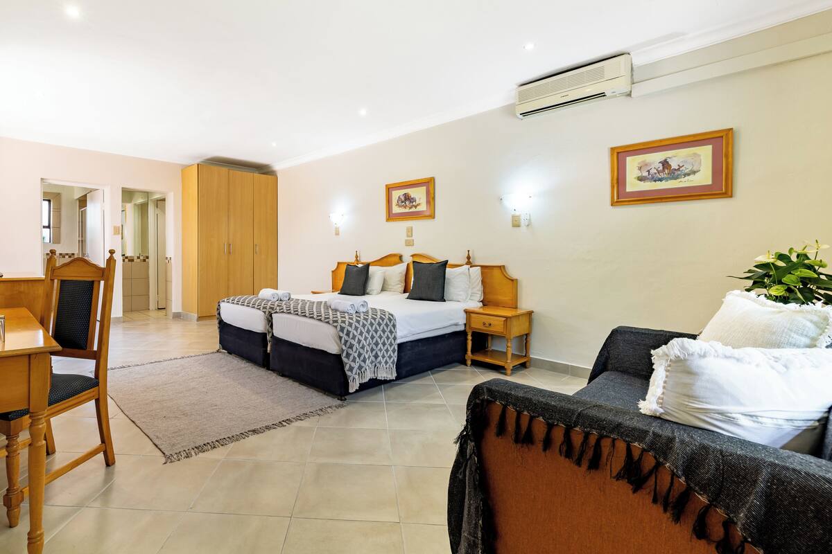 Une chambre d’hôtel comprenant un lit, un bureau avec une bouilloire, une chaise, un canapé et une plante en pot.