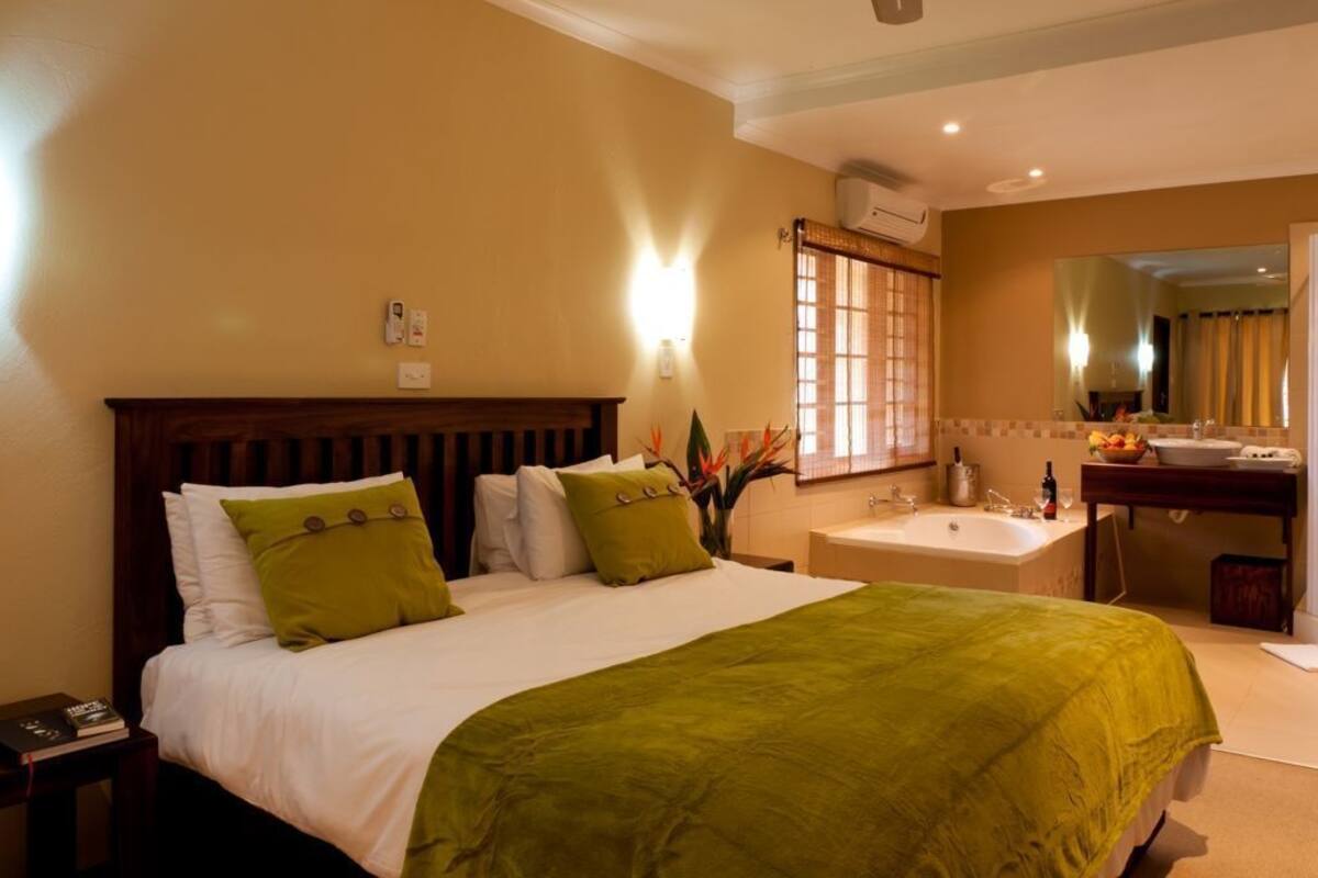 Une chambre d’hôtel comprenant un lit, une table de chevet, une lampe et une salle de bain avec un lavabo et un miroir.