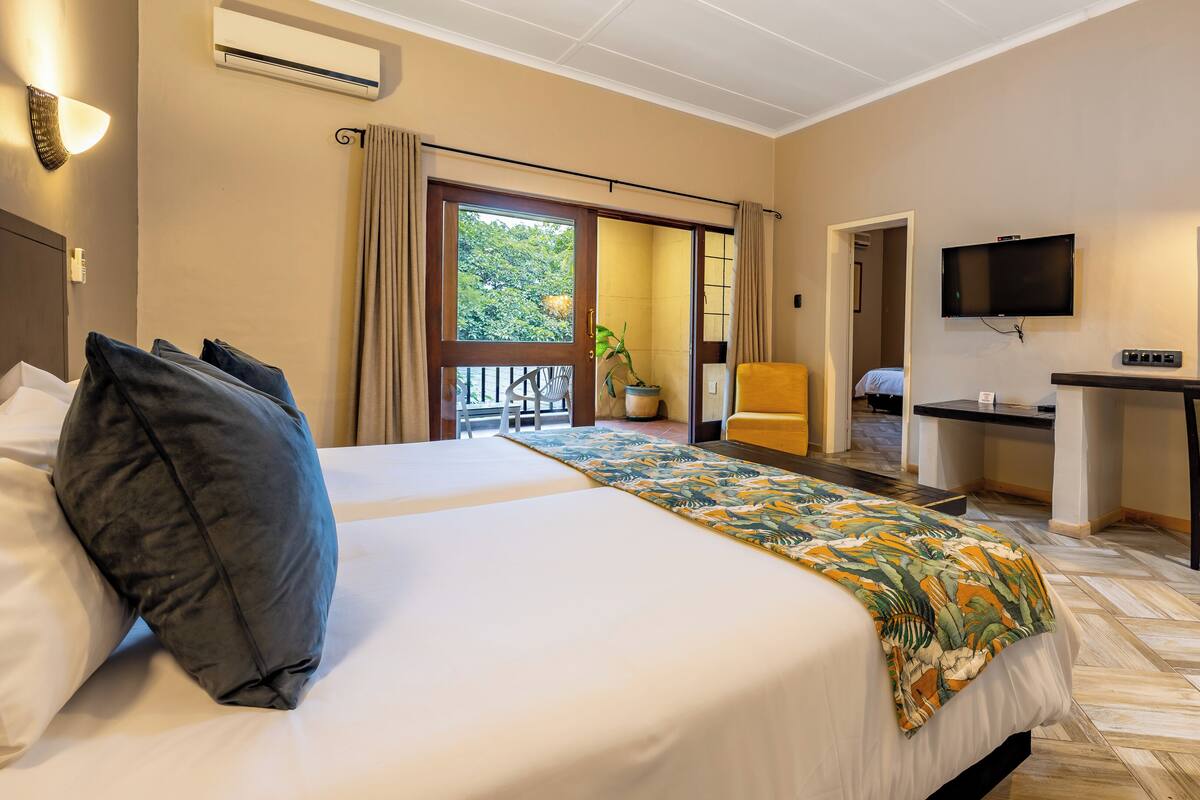 Une chambre d’hôtel avec un lit, un bureau, une télévision et un balcon avec des rideaux.