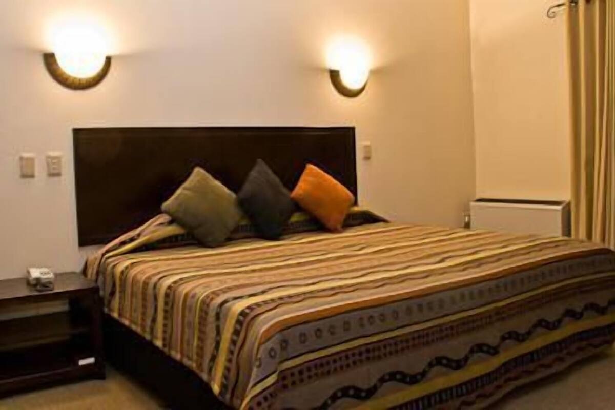 Une chambre à coucher avec un lit, deux tables de chevet et des lampes fixées au mur.